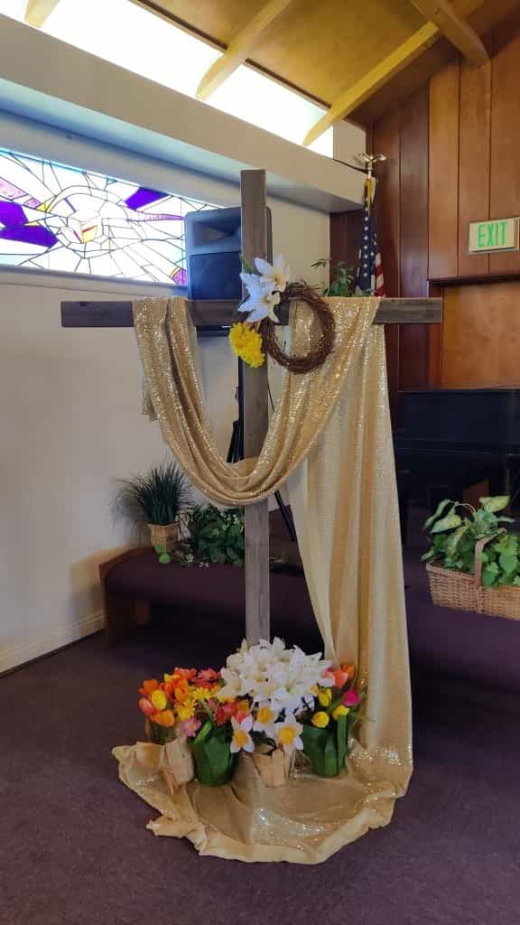A wooden cross with lilies, tulips, and gold cloth in the Cornerstone sanctuary.